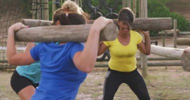 Acemi birliğinde egzersiz yapmaktan zevk alan, omuzlarında ağır çekimde tahta direklerle çömelmiş, çömelmiş vaziyette duran çok ırklı, mutlu bir kadın arkadaş grubunun yan görüntüsü.