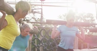 Çok ırklı, mutlu bir arkadaş grubunun yan görüntüsü. Acemi birliğinde egzersiz yapmaktan keyif alıyorlar. Omuzlarında tahta direklerle çömeliyorlar.