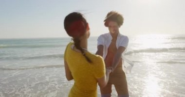 Deniz kenarında güneşli bir sahilde dans eden genç bir melez çiftin ön görüntüsü.