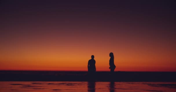 夕暮れ時にビーチで抱き合って走っているシルエットの若いカップルの正面ビュー — ストック動画