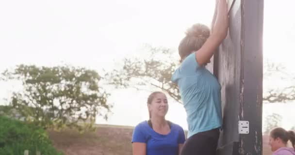 两个快乐的白人女人一起在新兵训练营做运动 一个帮助另一个女人爬过墙壁 背对着阳光 动作缓慢 — 图库视频影像