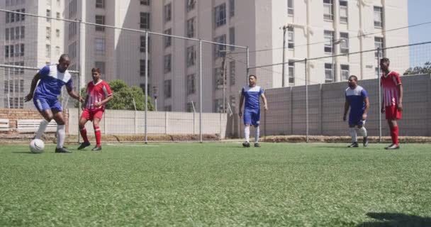 チームストリップを身に着けている男性サッカー選手の2つの多民族チームのフロントビュー 太陽の下でスポーツフィールドでのトレーニング 試合をプレイ ゴールを獲得 スローモーションで — ストック動画