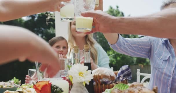 在一个阳光灿烂的日子里 在一个有着食物的菜园里 在一张桌子旁边 慢吞吞地举杯的多代白人家庭 在一起共度美好时光的侧视图 — 图库视频影像