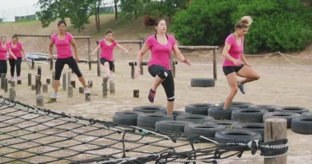 两个穿着粉色T恤衫的快乐的白人女人在训练营中一起锻炼 一起穿行轮胎 而其他女人则在后面慢吞吞地等着轮到她们 — 图库视频影像