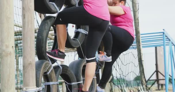ブートキャンプで一緒に運動を楽しんでピンクのTシャツを着て2つの幸せな白人女性の側面図 クライミングフレーム上のタイヤに登る スローモーションで — ストック動画