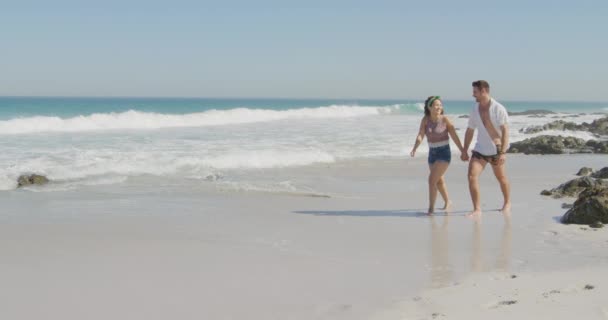 若い白人のカップルの正面ビューは 海で日当たりの良いビーチを歩いて無料の時間を楽しんでいます — ストック動画