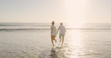 Genç melez çiftin deniz kenarında güneşli bir plajda koşup boş zamanlarının tadını çıkardığı arka manzara.