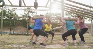 Acemi birliğinde egzersiz yapmaktan zevk alan, omuzlarında tahta direklerle çömelmiş, ağır çekimde çömelen mutlu, çok ırklı bir kadın arkadaş grubunun yan görüntüsü.