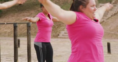 Acemi birliğinde egzersiz yapan, pembe tişört giyen ve ağır çekimde zıplayan çok ırklı bir kadın grubunun yan görüntüsü.
