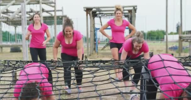 一群身穿粉色T恤衫的快乐的多民族女性在训练营地一起运动 等待轮到她们 并缓慢地爬到网下的镜头前 — 图库视频影像