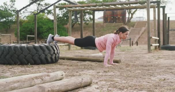 一个白人妇女在新兵训练营 用脚踏着轮胎做俯卧撑 慢动作时的侧视图 — 图库视频影像