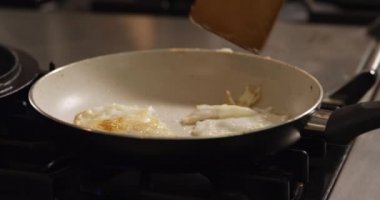 Spatula kullanan, mutfakta duran, kahvaltıyı hazırlayan, kızartma tavasında kızarmış yumurta yapan birinin ön tarafı..