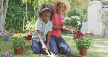 Afrika kökenli Amerikalı bir kadının bahçede iyi vakit geçirmesini, kızıyla birlikte diz çöküp çiçek dikmesini, güneşli bir günde, ağır çekimde gülmesini.