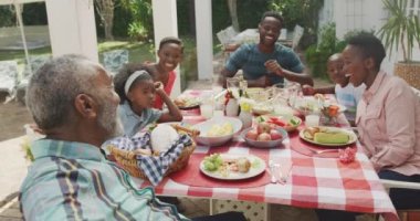 Çok nesilli çok ırklı bir ailenin birlikte iyi vakit geçirmesini, bahçesinde yemek olan bir masada oturmasını, akıllı telefon tutan, güneşli bir günde ailesiyle selfie çeken yaşlı bir adamın yan görüntüsü.