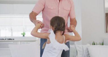 Yan görüntüde, kıdemli beyaz bir adam dairesinde eğleniyor, torunuyla dans ediyor, el ele tutuşuyor, ağır çekimde.