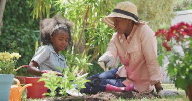 Afrika kökenli Amerikalı bir kadının bahçede iyi vakit geçirmesini, diz çöküp konuşmasını, güneşli bir günde yavaş çekimde kızına öğüt vermesini.
