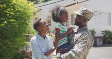 Afrika kökenli Amerikalı bir ailenin bahçede vakit geçirmesinin yan görüntüsü. Bir adam askeri üniforma giyiyor, kızını tutuyor, güneşli bir günde, ağır çekimde ona bakıyor.