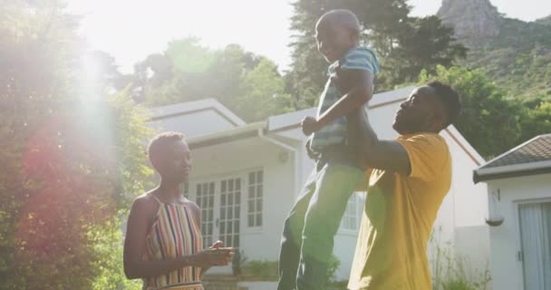 在阳光灿烂的日子里 一个黑人家庭一边欣赏着他们在花园里度过的时光 一边抬举他的儿子 慢慢地把他放在肩上 — 图库视频影像