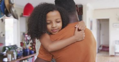 Afrika kökenli Amerikalı bir adam ve melez kızının evde birlikte vakit geçirmesinin arka planında bir adam kızını kucağında tutuyor ve gülümsüyor.