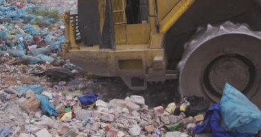 Çalışan ve çöpleri temizleyen aracın yan görüntüsü. Çöp dolu bir çöp yığını üzerinde ağır çekimde çalışan ve çöpleri temizleyen araçlar.