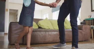 Afro-Amerikalı bir adam ve melez kızının yan görüntüsü. Evde birlikte vakit geçiriyorlar. Dans ediyorlar, el ele tutuşuyorlar, gülümsüyorlar.