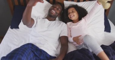 Afrika kökenli Amerikalı bir adam ve melez kızının evde birlikte vakit geçirmesi, yatakta uzanması, kızın oyuncak ayıyı tutması ve erkeğin yavaş çekimde selfie çekmesi.