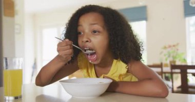 Melez bir ırk kızının evdeki zamanının tadını çıkarması, masada oturması, kahvaltıda gevrek yemesi, ağır çekimde.