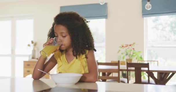 家で彼女の時間を楽しんで混合レースの女の子のフロントビュー テーブルに座って 朝食を食べます ジュースを飲みます スローモーションで — ストック動画