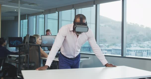 現代のオフィスで働いているアフリカ系アメリカ人ビジネスマンの正面図 Visual Realityヘッドセットを身に着けており 同僚とスローモーションの背景で働いています — ストック動画