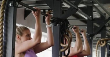 Spor kıyafetleri giyen beyaz bir kadın ve erkek spor salonunda yan yana antrenman yaparken, barfiks çekerken, ağır çekimde barfiks çekerken.