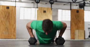 Spor kıyafetleri giyen beyaz bir adamın spor salonunda çapraz antrenman yaparken, halterlerle ağırlık antrenmanı yaparken, dambılları tutarken ve yedek ağırlık kaldırırken ön görüntüsü.