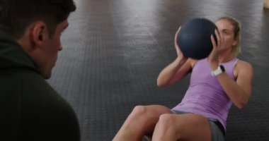 Spor kıyafetleri giyen, elinde sağlık topu tutan, mekik çeken ve oyuncak topunu kafasının üstüne kaldıran, ayaklarını ağır çekimde tutan bir posta eğitmeni olan beyaz atletik bir kadının ön görüntüsü.