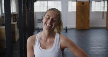 Çekici, mutlu, atletik, sarı saçlı, atkuyruklu beyaz bir kadının portresi. Spor salonunda antreman yapıyor, kameraya bakıyor ve gülümsüyor.