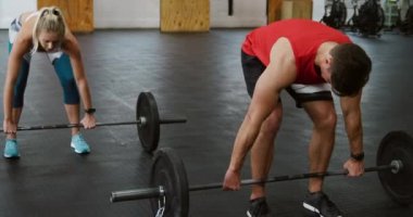 Spor kıyafetleri giyen beyaz bir erkek ve kadının spor salonunda ayakta durup ağırlık çalışması yaparken, onları yerden kaldırırken ve kafalarının üstünde göğüs seviyesinden yükseltirken ön görüntüsü.