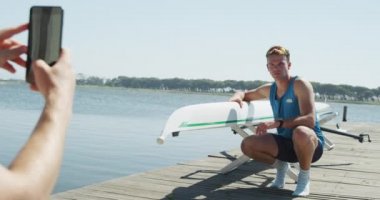 Kafkas erkek kürekçinin, güneşli bir günde, ağır çekimde çömelmiş, elinde tekne tutan beyaz bir kürekçinin fotoğrafını çekerken omuz hizasında.