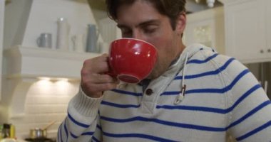 Kafkasyalı bir adamın dairede vakit geçirmesinin ön görüntüsü, bir masa başında, elinde bir fincan çay, içki, ağır çekimde. Karantina karantinasında sosyal uzaklık ve kişisel izolasyon