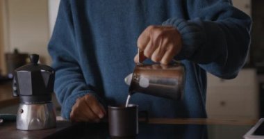 Sosyal uzaklık ve kendini karantinaya alma. Üst düzey beyaz bir kadının mutfağında dinlenirken, tezgahta durup kahve yaparken, sütü sürahisinden bardağına dökerken, ağır çekimde...