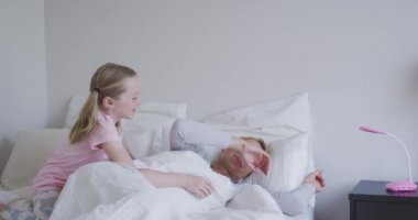 Kafkasyalı mutlu bir kadın kızıyla birlikte evde vakit geçiriyor, yataklarında uzanıyor, onu uyandırıyor, gülümsüyor ve birbirlerine bakıyor, sosyal mesafeler ve karantina tecridinde, yavaş çekimde kendini izole ediyor..