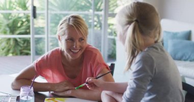 Mutlu, beyaz bir kadın kızıyla birlikte evde vakit geçiriyor, oturma odasında bir masada oturuyor, resim yapıyor, gülümsüyor ve birbirlerine bakıyor, burnunu boyuyor, sosyal mesafe koyuyor ve karantinada kendini izole ediyor.