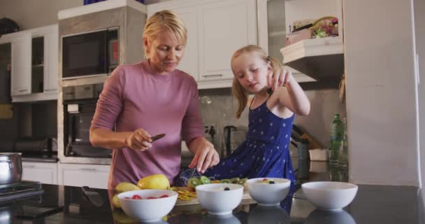 一緒に家で娘と家族の時間を楽しんで幸せな白人女性 フルーツサラダを準備し 彼らの台所で笑顔 隔離されたロックダウンでの社会的距離と自己分離 スローモーションで — ストック動画
