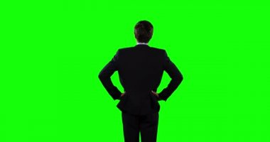 Kafkasyalı bir işadamının arkadan görünüşü, kısa saçlı, şık kıyafetler giyen, elleri kalçasında duran, yeşil ekran arka planında duran.