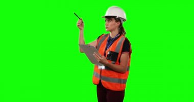 Kafkaslı, yüksek görüş açısına sahip yelek giyen beyaz bir kadının yeşil ekran arka planındaki bir klasöre bir numara yazıp sayması..