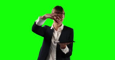 Beyaz tenli, uzun siyah saçlı, şık kıyafetler giyen, yeşil perde arkasında elinde dijital tabletle gezen bir iş kadınının ön görüntüsü..