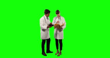 Laboratuvar önlüğü ve steteskop giyen, tablet kullanan, yeşil ekran arkaplanındaki notları kontrol eden iki beyaz erkek ve kadın doktorun ön görüntüsü..