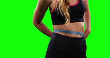 Formda, sportif kıyafetler giyen ve yeşil ekran arka planında ölçü bandıyla belini ölçen bir ırk kadınının ön görüntüsü..