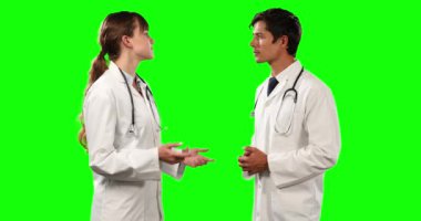 Yan görüntüde iki beyaz erkek ve kadın doktor laboratuvar önlüğü ve stetoskop giyiyorlar, duruyorlar ve konuşuyorlar, yeşil ekran arka planında..