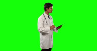 Beyaz bir erkek doktorun laboratuvar önlüğü ve steteskop giyip yeşil ekran arka planında tablet kullanırken yan görüntüsü..