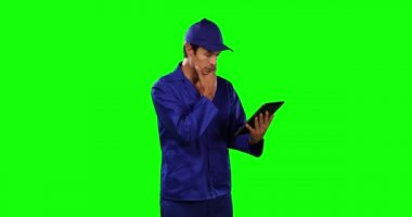 Kafkasyalı, kısa siyah saçlı, elinde dijital tablet, iş kıyafetleri ve yeşil ekran arka planı olan beyaz erkek bir araba tamircisinin yan görüntüsü.