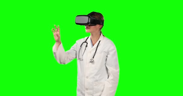 Vorderansicht einer kaukasischen Ärztin mit Laborkittel und Virtual-Reality-Brille, die auf einen virtuellen Bildschirm auf grünem Hintergrund zeigt.