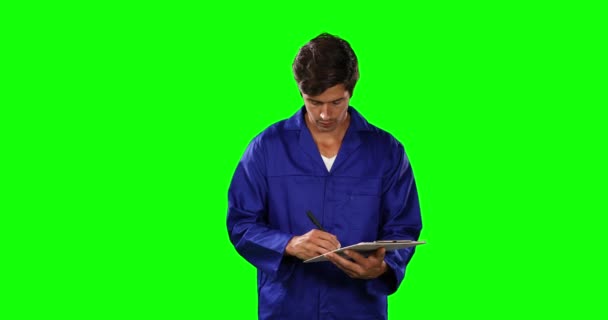 一位快乐的高加索男性工程师的侧视图 他是一位汽车修理工 留着短短的黑发 站在文件夹里写字 穿着工作服 在绿色的背景下微笑着 — 图库视频影像